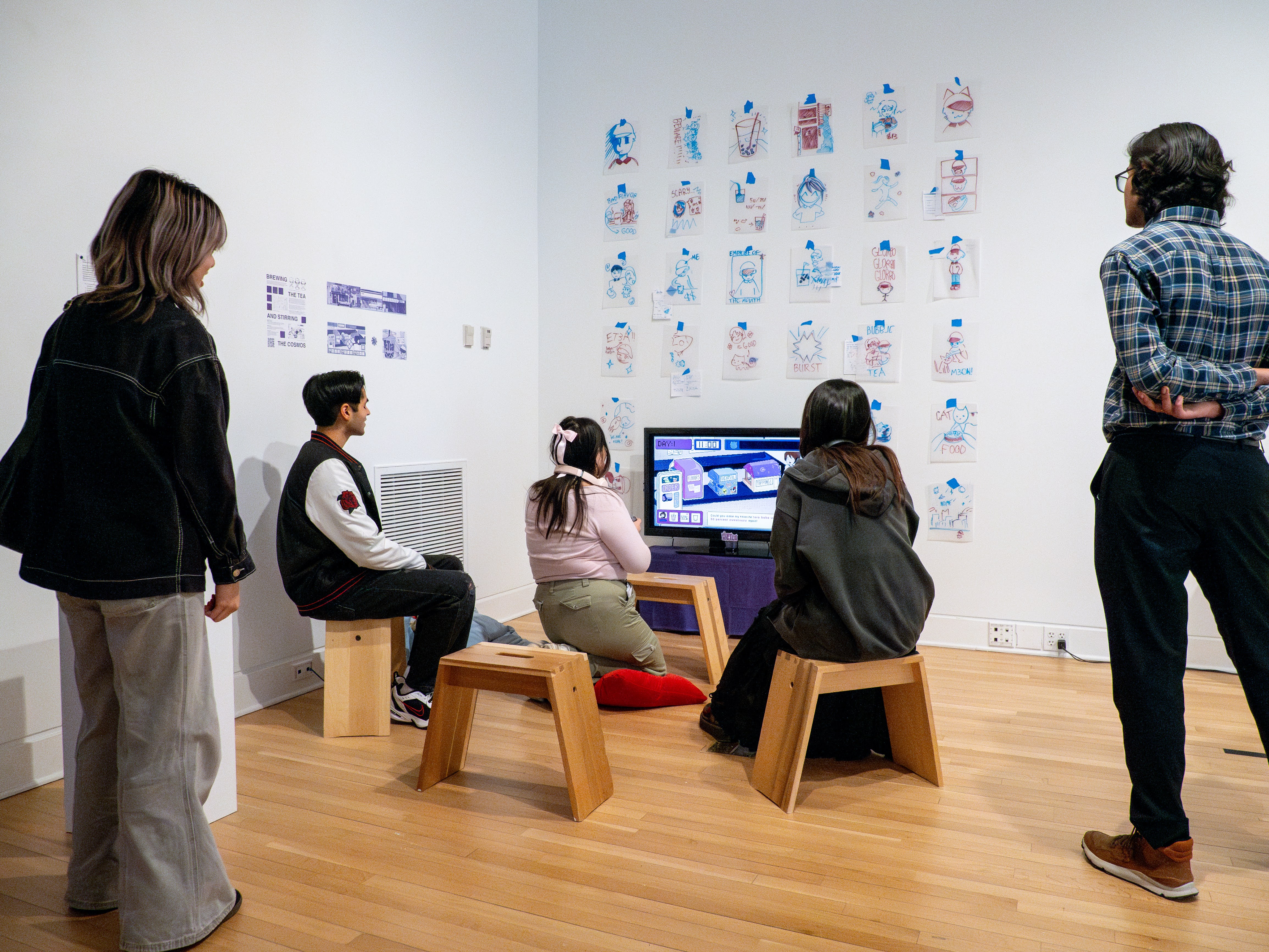 A group of people huddled around a TV, playing a video game. The room is bright, and the walls are covered with drawings.