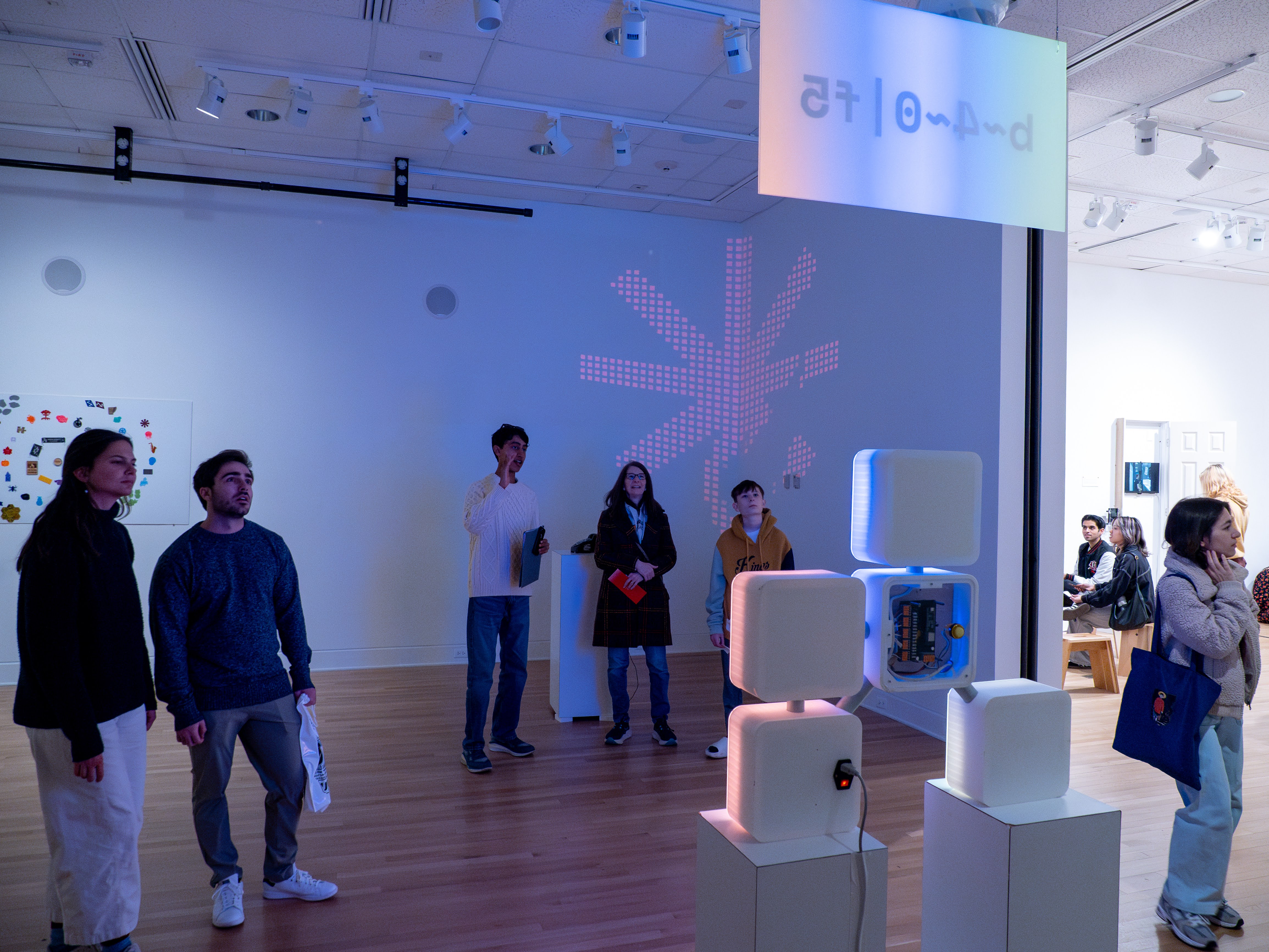 Two groups of people are looking at a meter-tall LED sign, which is glowing with colors. The room is dark, but you can see the edge of the bright room.